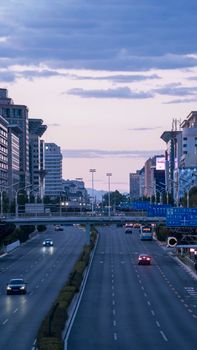 Dusk view of an urban road with buildings and cars, set against a twilight sky.