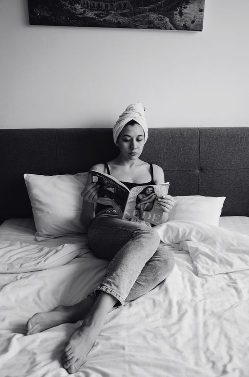 Free A woman relaxes with a magazine in a cozy bedroom setting, wrapped in a towel. Stock Photo