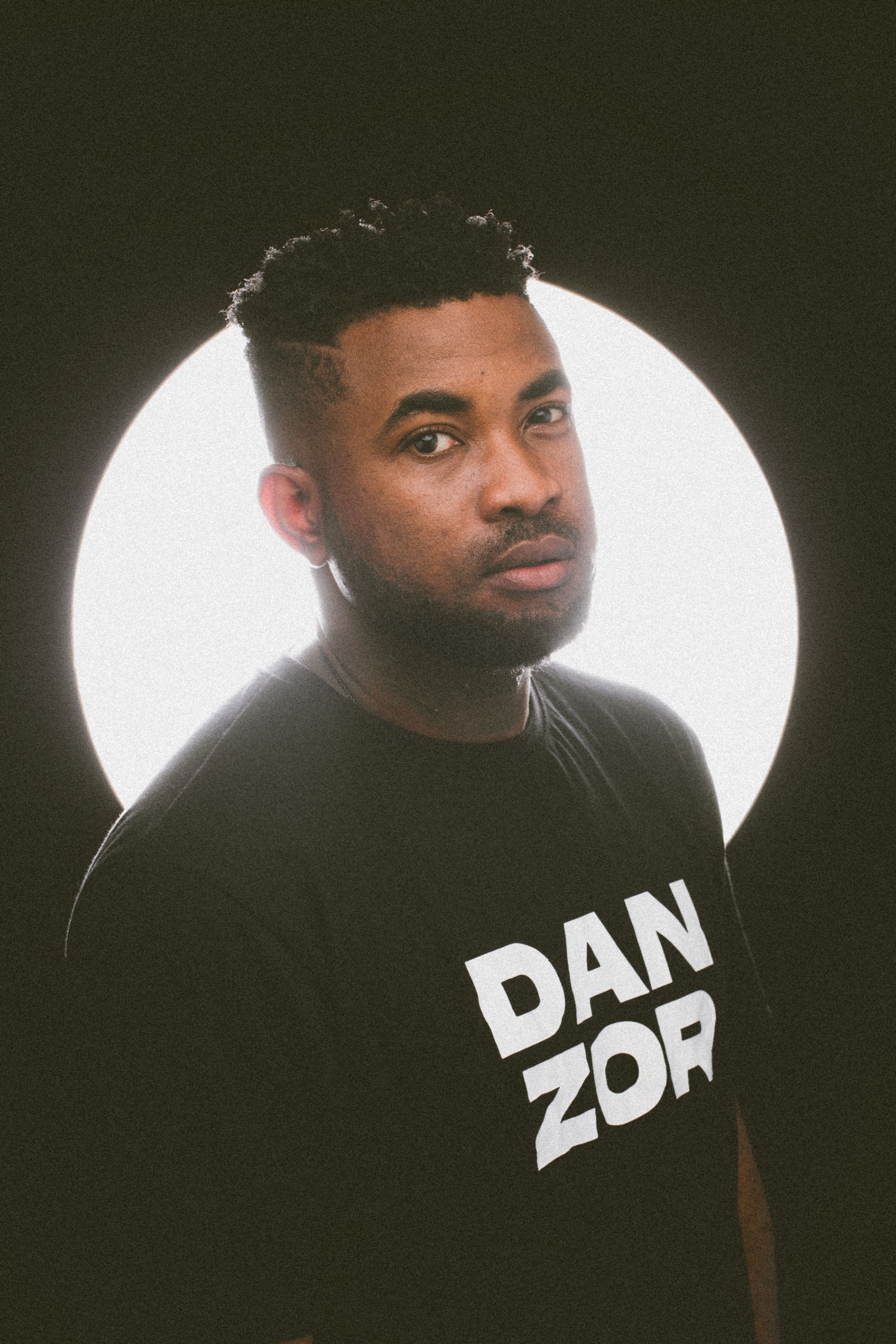 Studio portrait of an African American man wearing a black graphic t-shirt with a halo lighting effect.