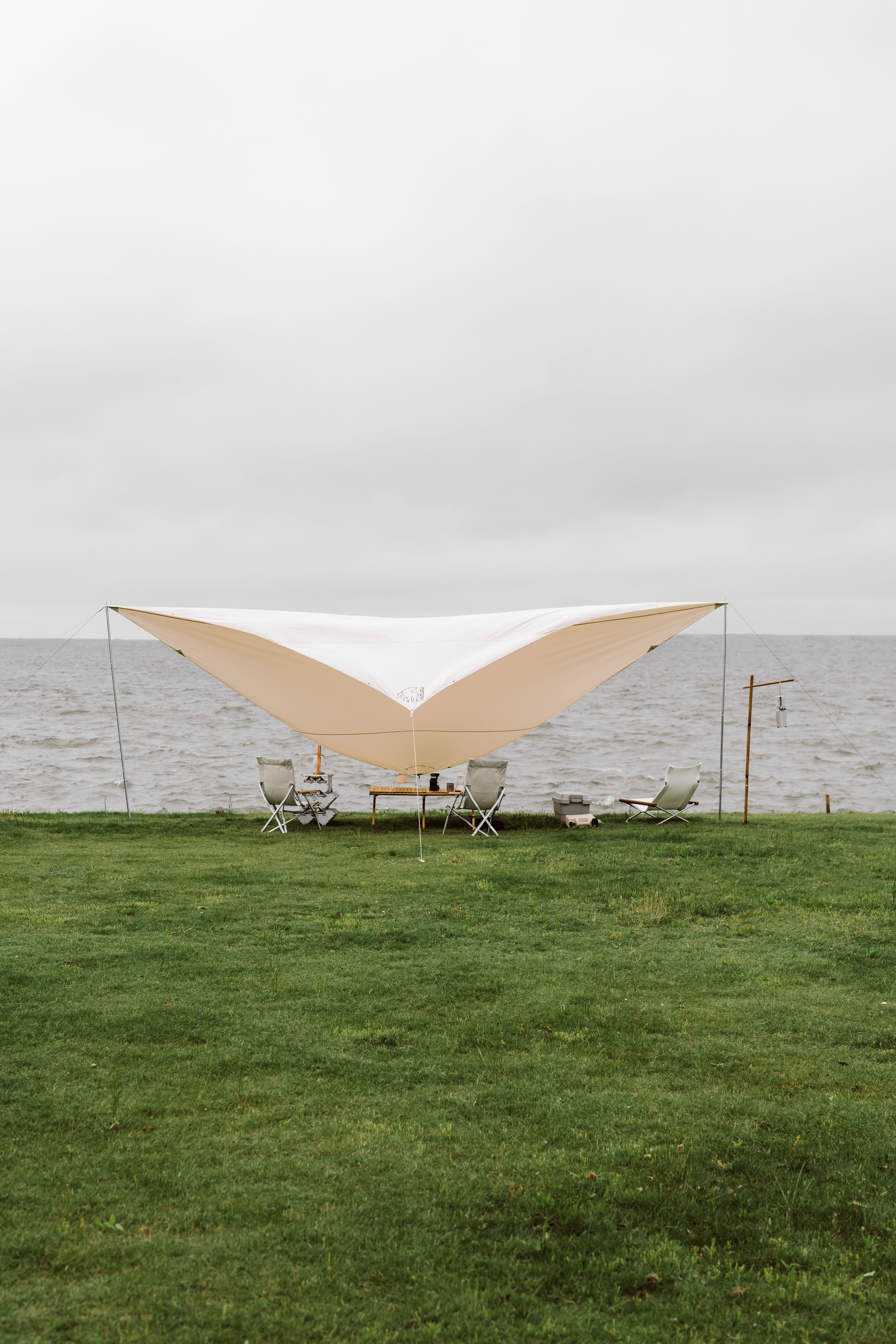 Flat lay of camping layers, rain jacket, tarp, and tent stakes on a picnic table with a cloudy sky in the background