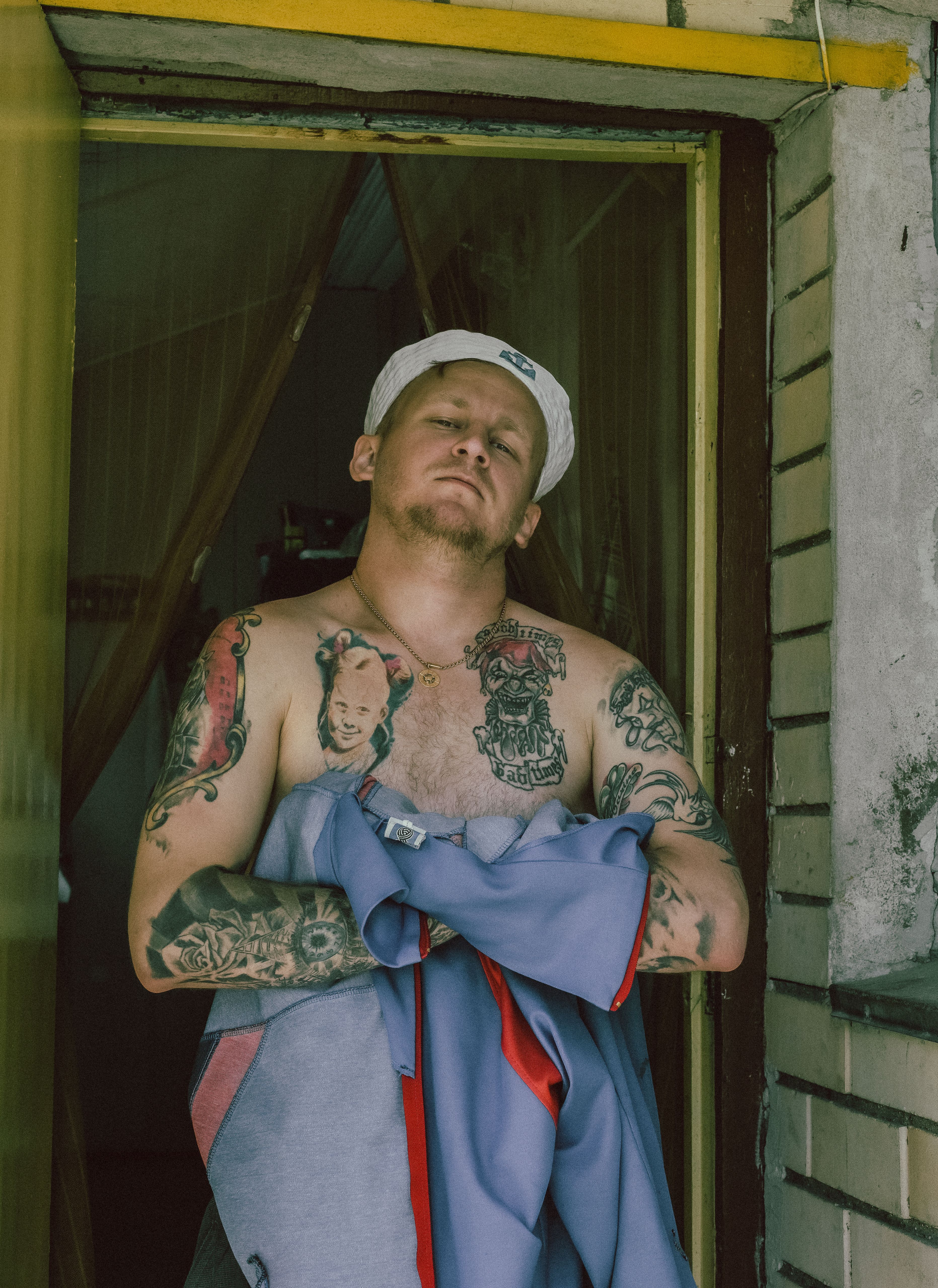 Young tattooed man in doorway holding clothes with confident expression, embracing subculture style.