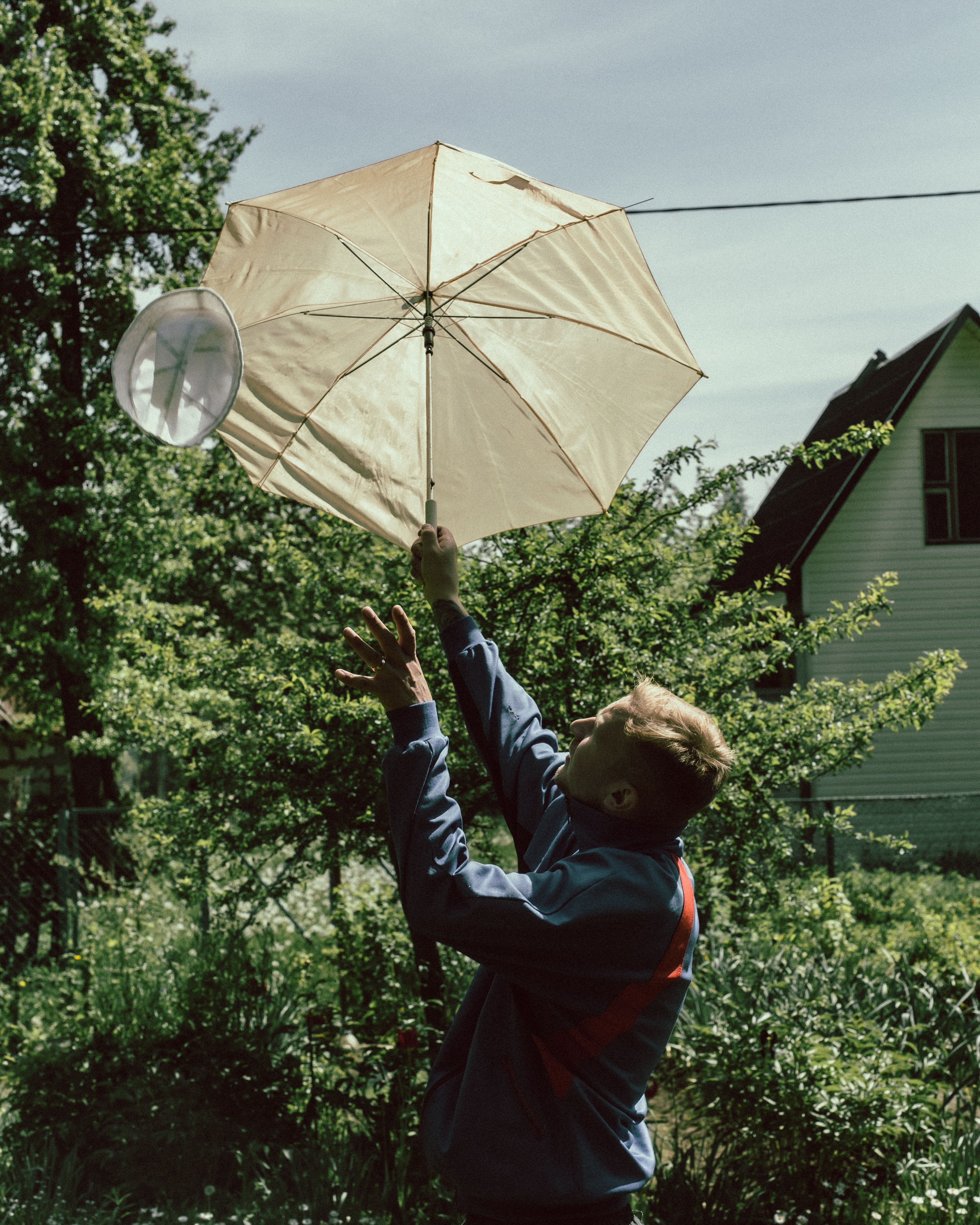 A man in a blue jacket holds an umbrella against a garden backdrop, creating a playful scene.