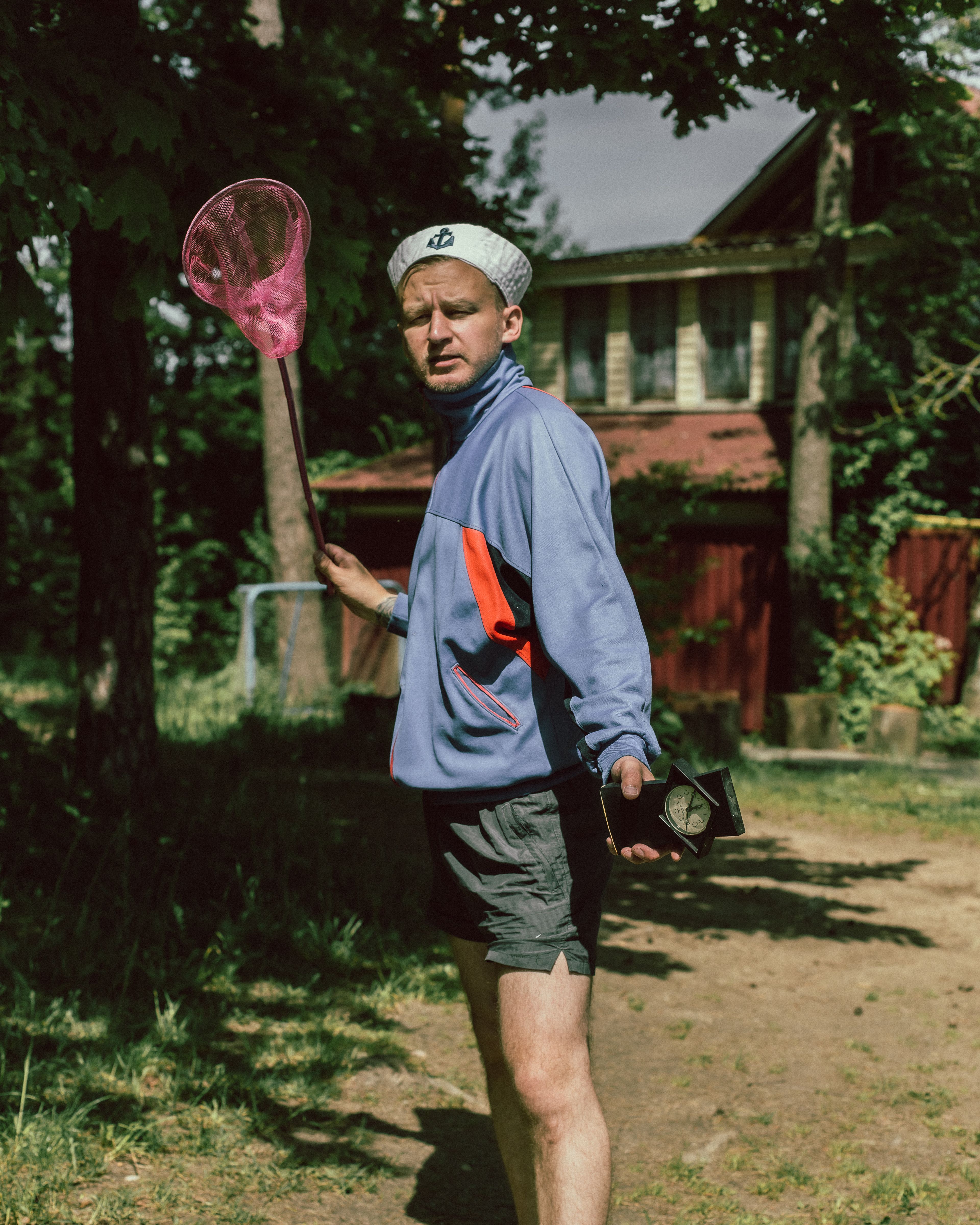 Man in casual attire holding a pink catching net outdoors on a sunny day.