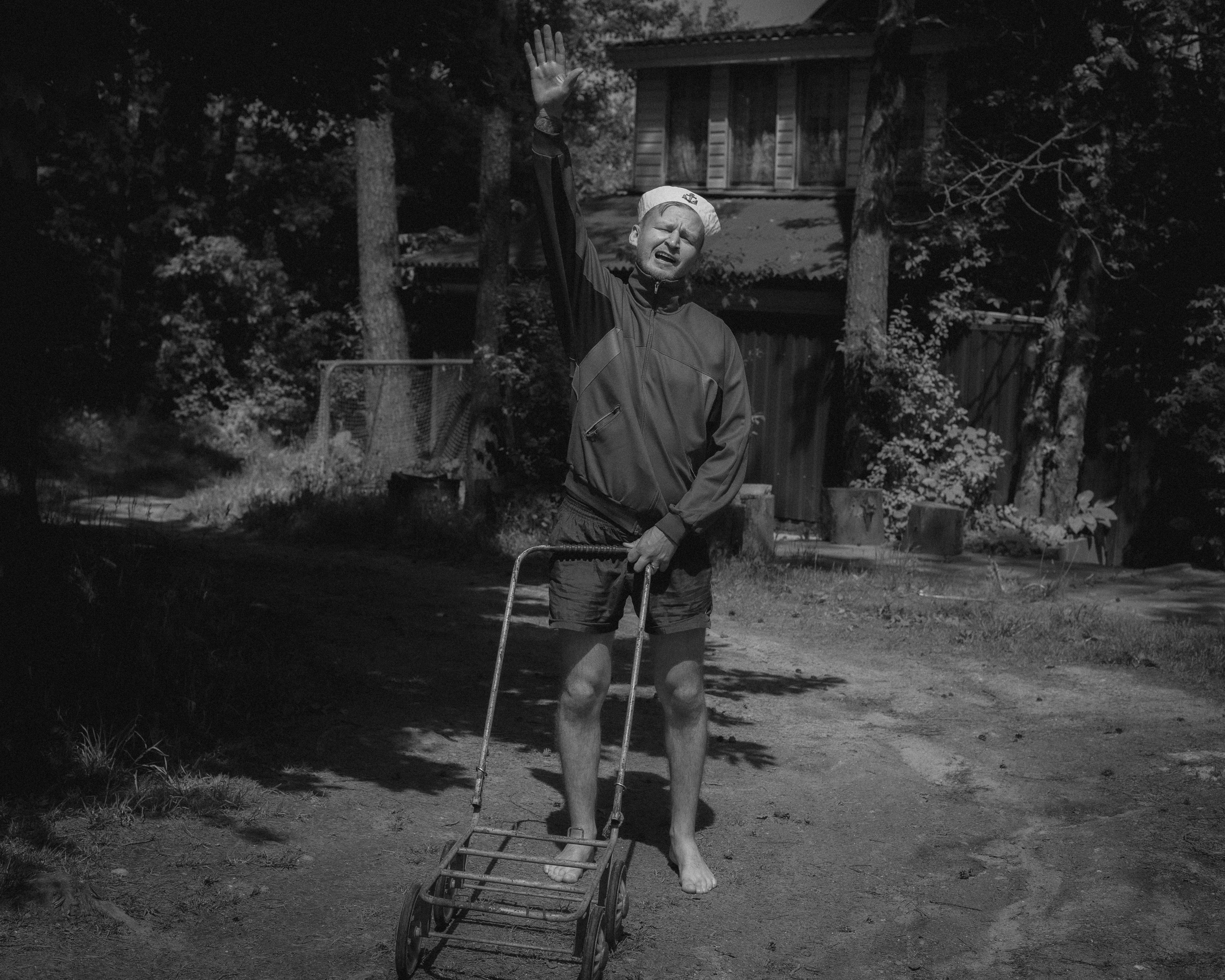Elderly man in shorts raising hand in sun-dappled garden, monochrome image.