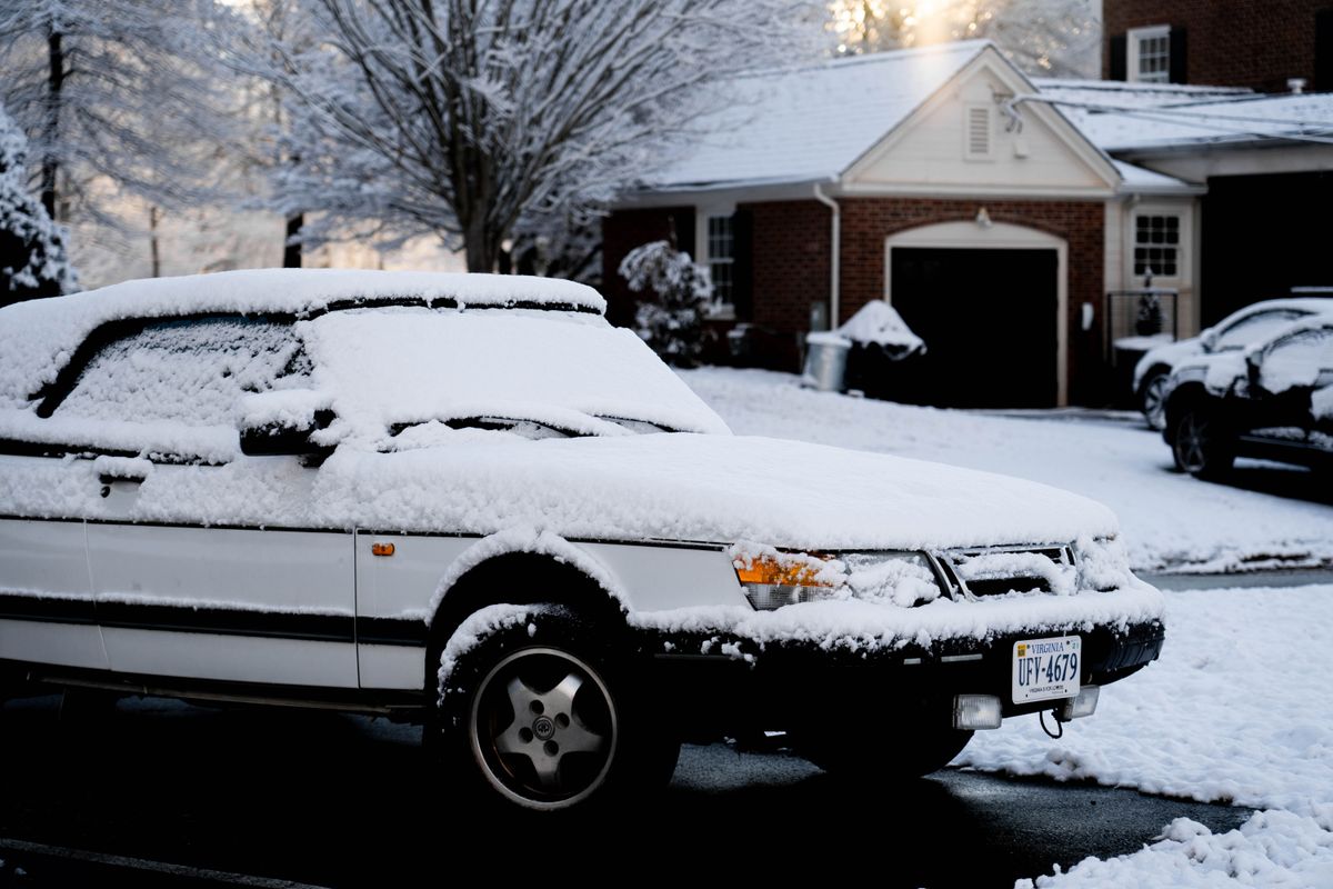 A snow-covered car parked on a residential street during the season's first cold snap