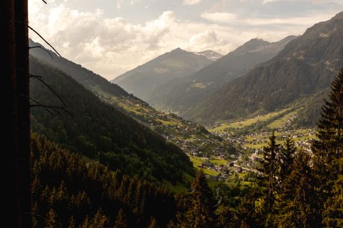 Free Scenic view of a serene mountain village nestled in a lush green alpine valley under a cloudy sky. Stock Photo