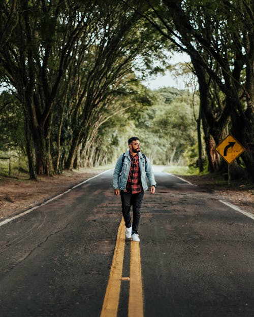 Full Shot of a Man in Denim Jacket and Black Pants Walking on Concrete Road