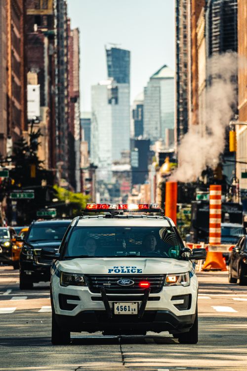 Free A New York police car navigates through a bustling urban street with skyscrapers in the background. Stock Photo