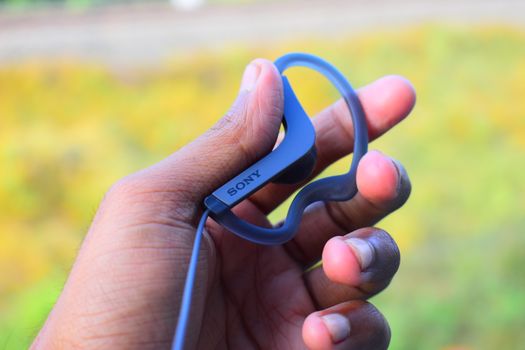 Detailed close-up of a hand holding stylish wireless earphones outdoors.