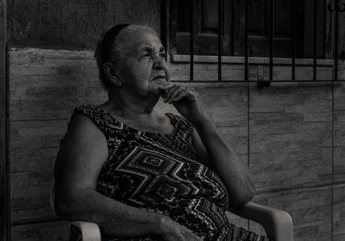 Free Elderly woman sitting thoughtfully in grayscale portrait outdoors. Stock Photo