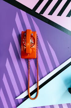 Bright orange rotary phone on a colorful geometric wall, capturing retro aesthetics and vibrant style.