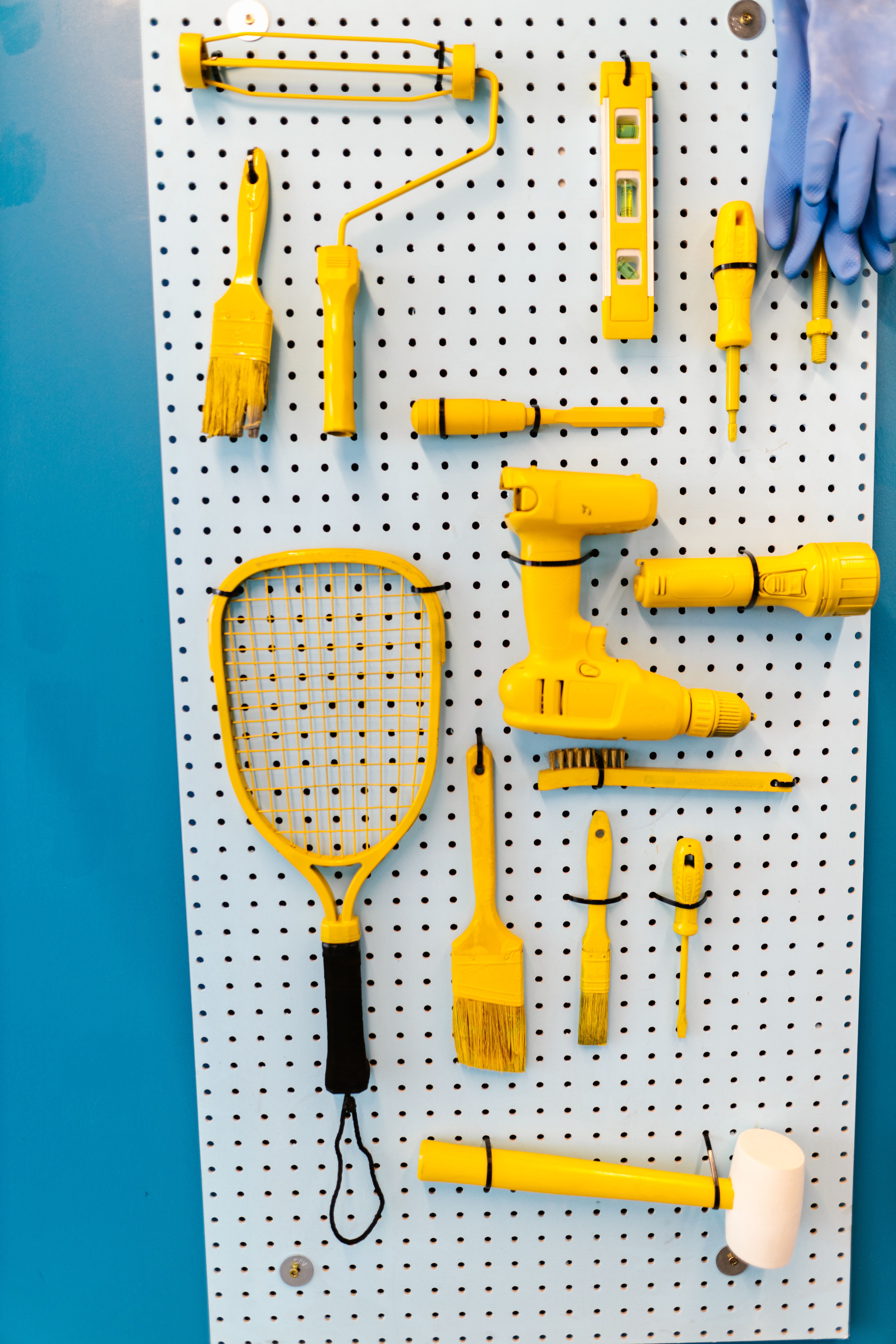 An assortment of yellow tools organized neatly on a white pegboard with blue background.