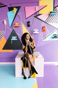 A stylish woman posing with vintage phones on a colorful geometric wall.