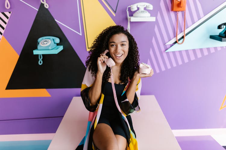 Woman Sitting, Smiling And Holding A Retro Phone 