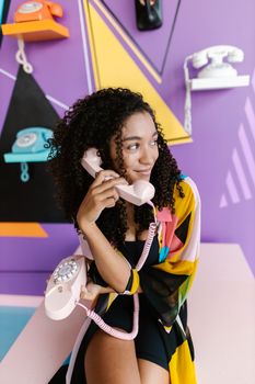 Stylish woman holding a pink rotary phone against a colorful geometric backdrop.