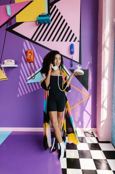 A woman stands in a vibrant, retro-themed room with vintage telephones on the wall.