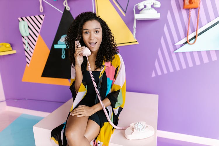 Woman Sitting With Telephones Around And On Wall