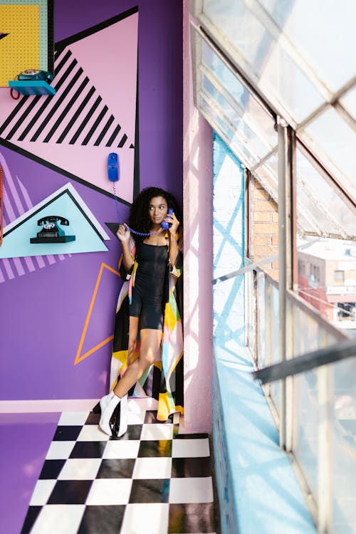 Woman Holding a Vintage Phone and Standing in Front of a Colorful Wall with Vintage Phones