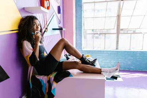 Woman Holding a Vintage Phone and Sitting in Front of a Colorful Wall with Vintage Phones