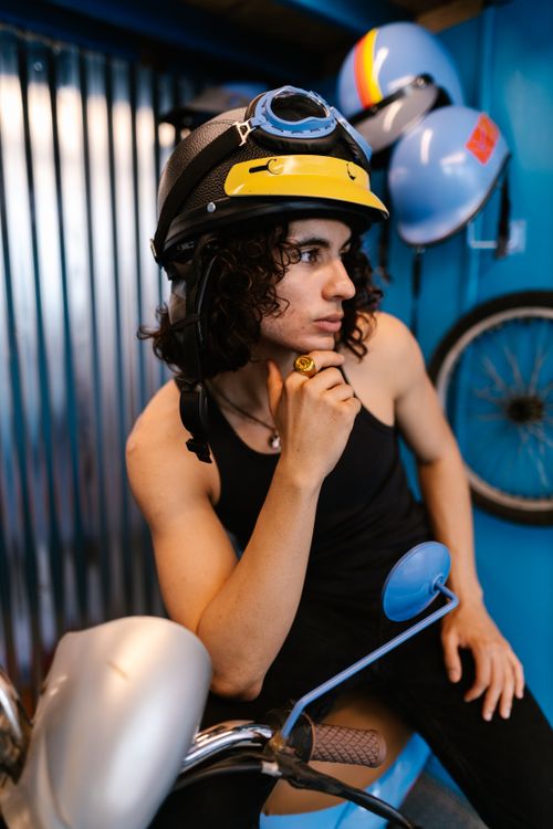 Free Young man in retro helmet and tank top sitting on a motor scooter inside a garage. Stock Photo