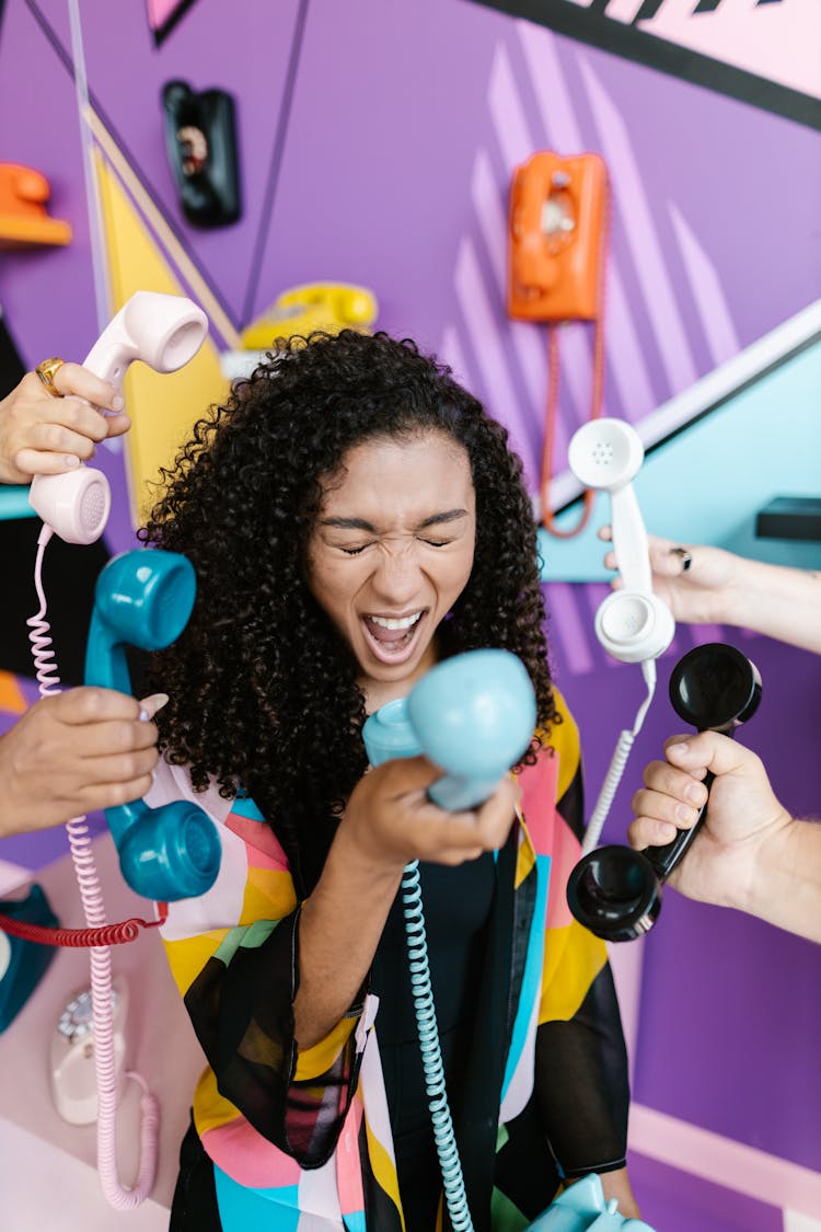 Woman Screaming To A Vintage Phone In Front Of A Colorful Wall With Vintage Phones