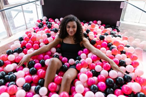 Free Cheerful woman relaxing in colorful pink, black, and white ball pit, capturing joy and leisure indoors. Stock Photo