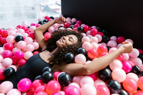 Free Smiling woman relaxing with closed eyes in a colorful ball pit indoors. Stock Photo