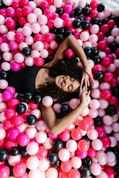 Free Joyful woman lying in a vibrant ball pit of pink and black balls, smiling and relaxed. Stock Photo