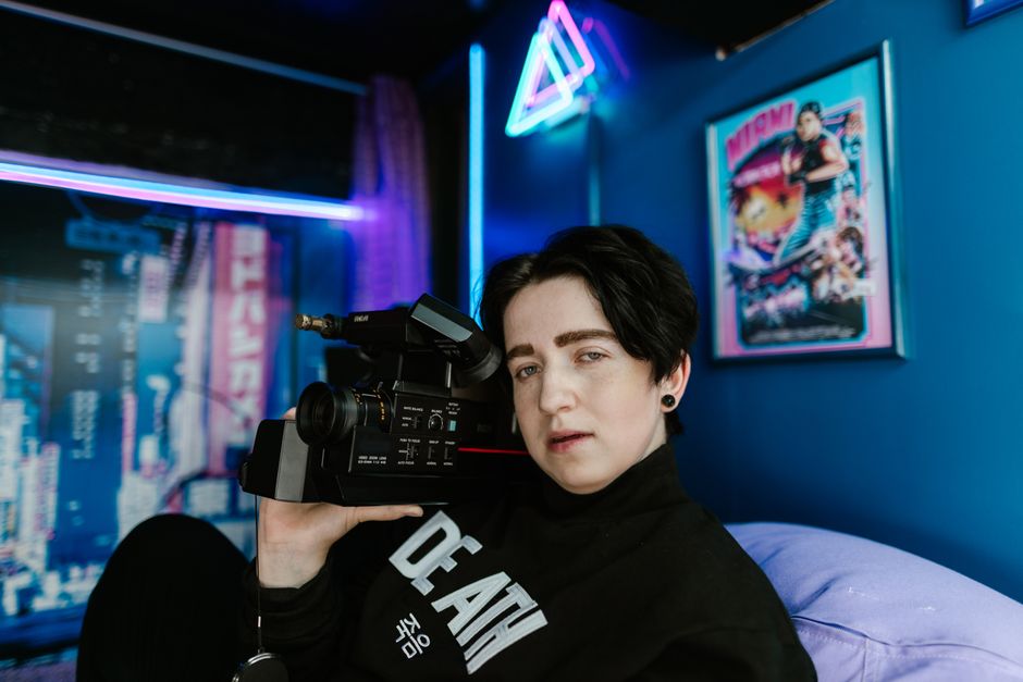 Cyberpunk decor style interior — Portrait of a person holding a vintage camcorder in a neon-lit room, capturing a retro vibe.