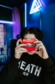 Young adult exploring a vintage red 3D viewer in a neon-lit room, highlighting technology nostalgia.