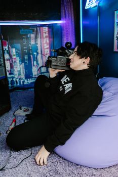 Young adult using a vintage camera on a bean bag in a neon-lit room.