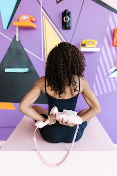 Back view of a woman holding a vintage phone in a colorful retro-themed studio setup.