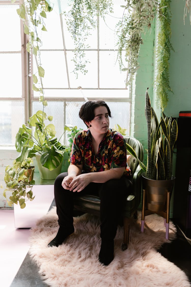 Gen Z Guy Sitting In Chair In Plants Interior