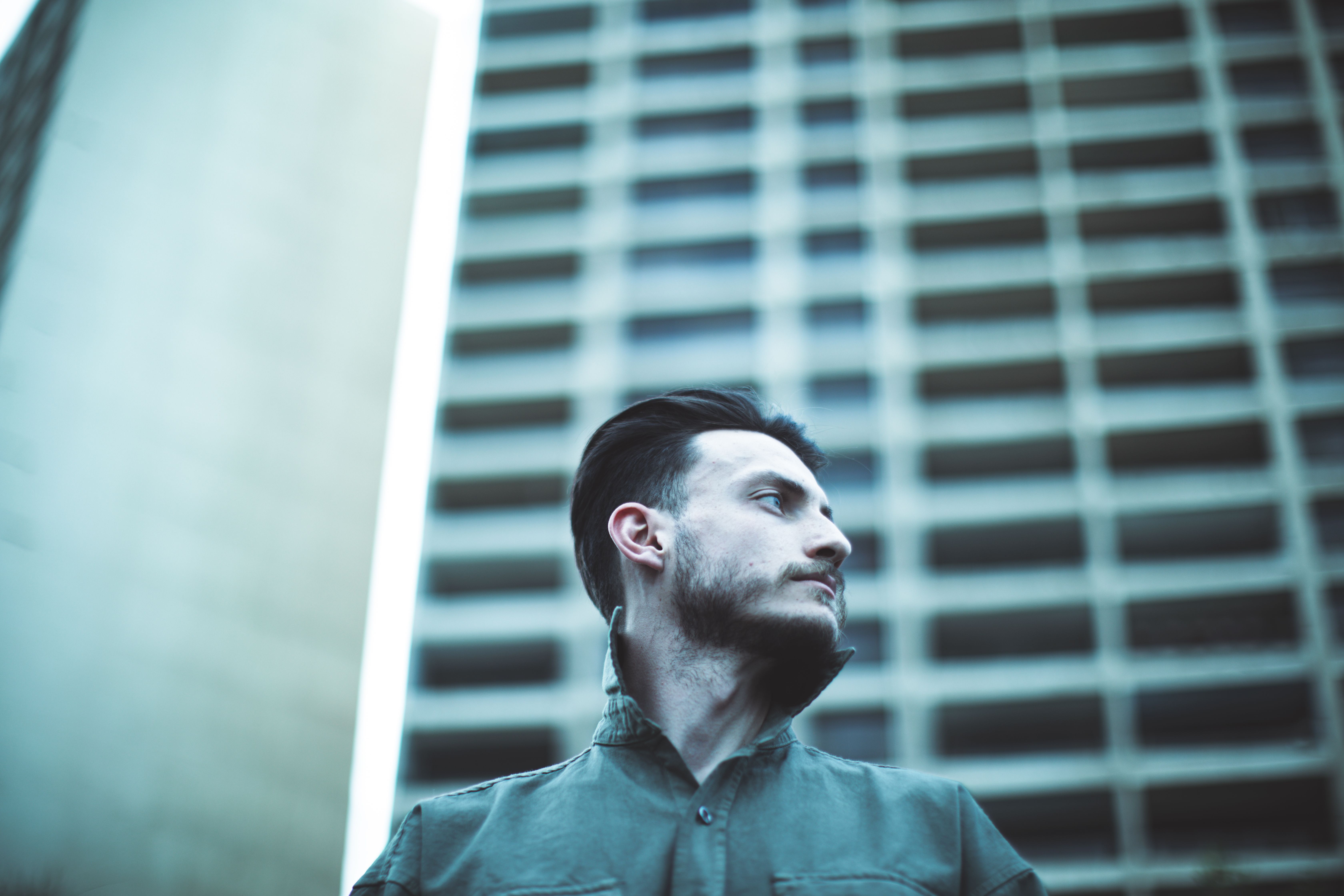 Low-angle portrait of a bearded man looking sideways against a modern urban background.