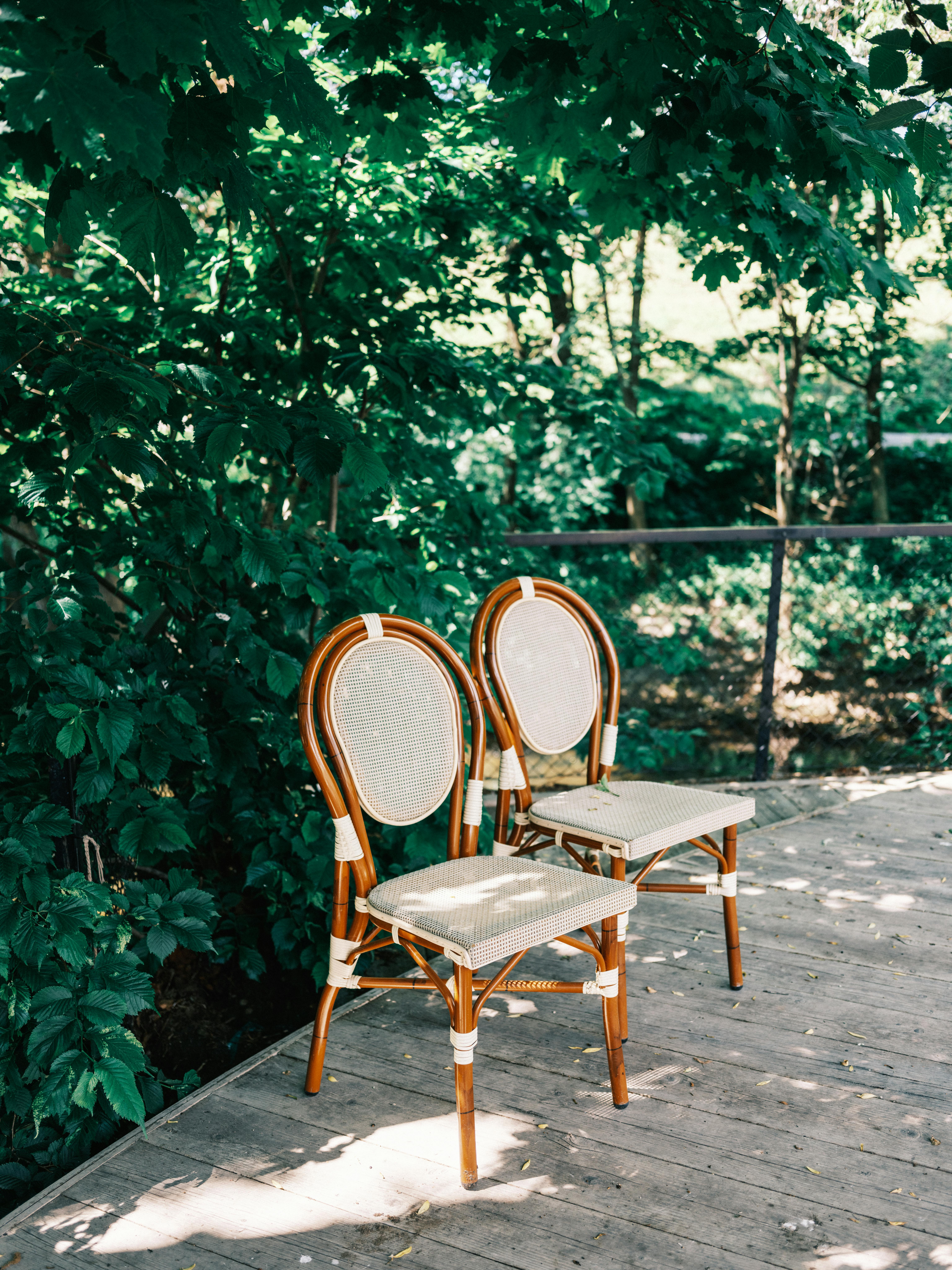 Two elegant wooden chairs on a sunny wooden deck amidst lush greenery.