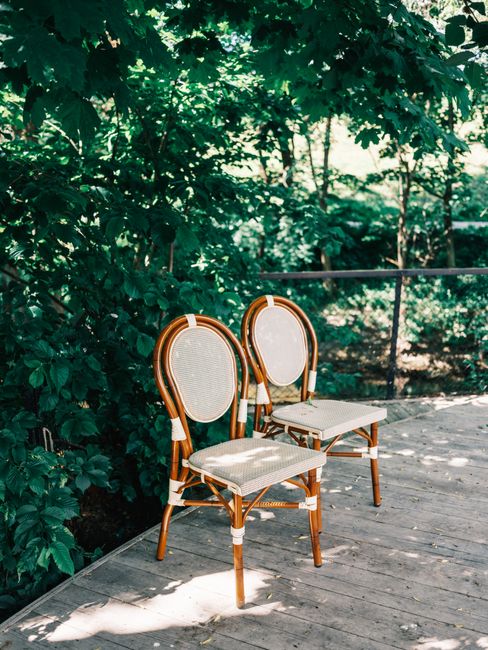 Two elegant wooden chairs on a sunny wooden deck amidst lush greenery.