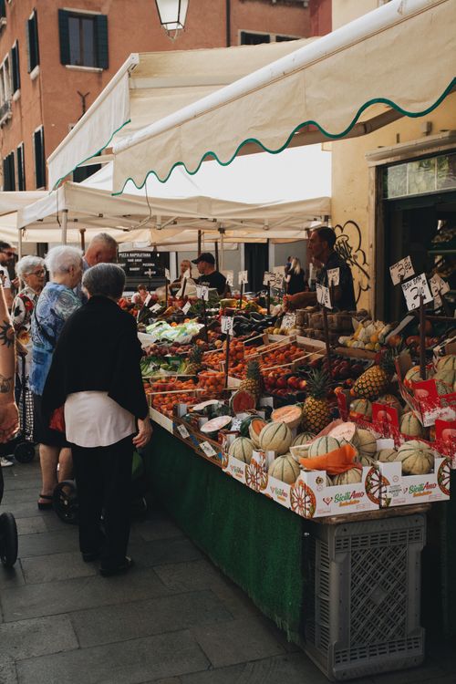Free Colorful street market in Italy with fresh produce and people shopping under awnings. Stock Photo