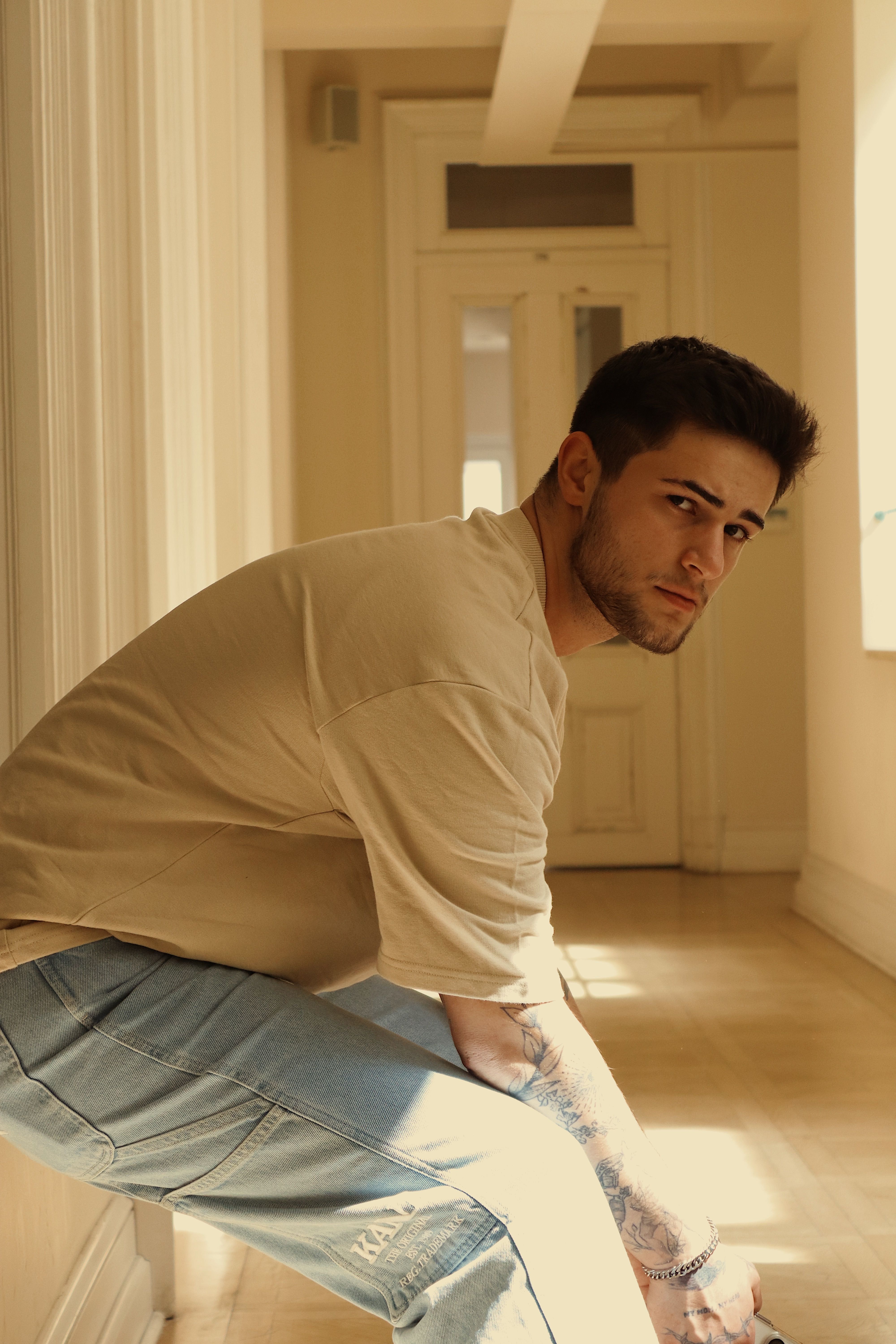 Profile of a young man in casual clothing posing indoors with natural sunlight.