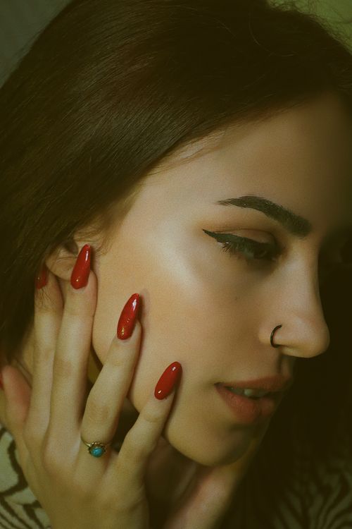 Free Close-up portrait of a stylish young woman with red nails and nose ring, embodying modern beauty and fashion. Stock Photo