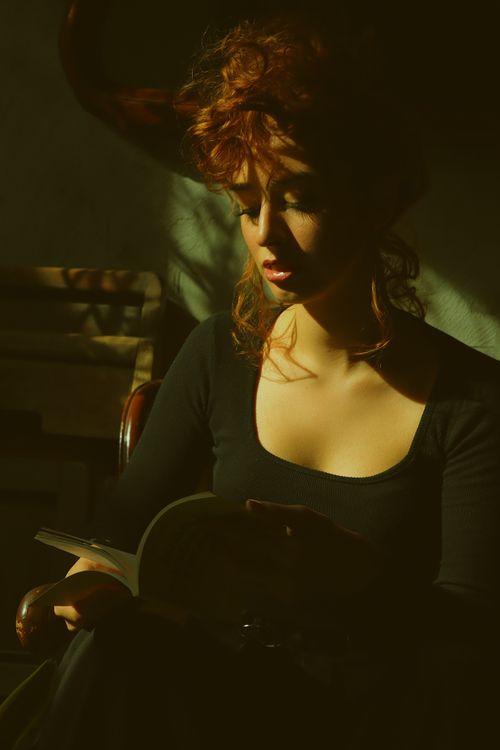 Free Elegant portrait of a woman in a black long sleeve reading indoors, captured in soft, dramatic lighting. Stock Photo
