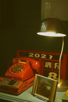 A nostalgic desk setting featuring a vintage rotary phone, illuminated lamp, and retro calendar.