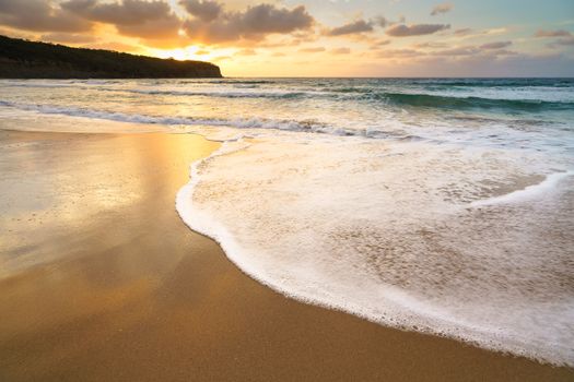 Serene beach scene at sunset in Australia with waves gently reaching the sandy shore.