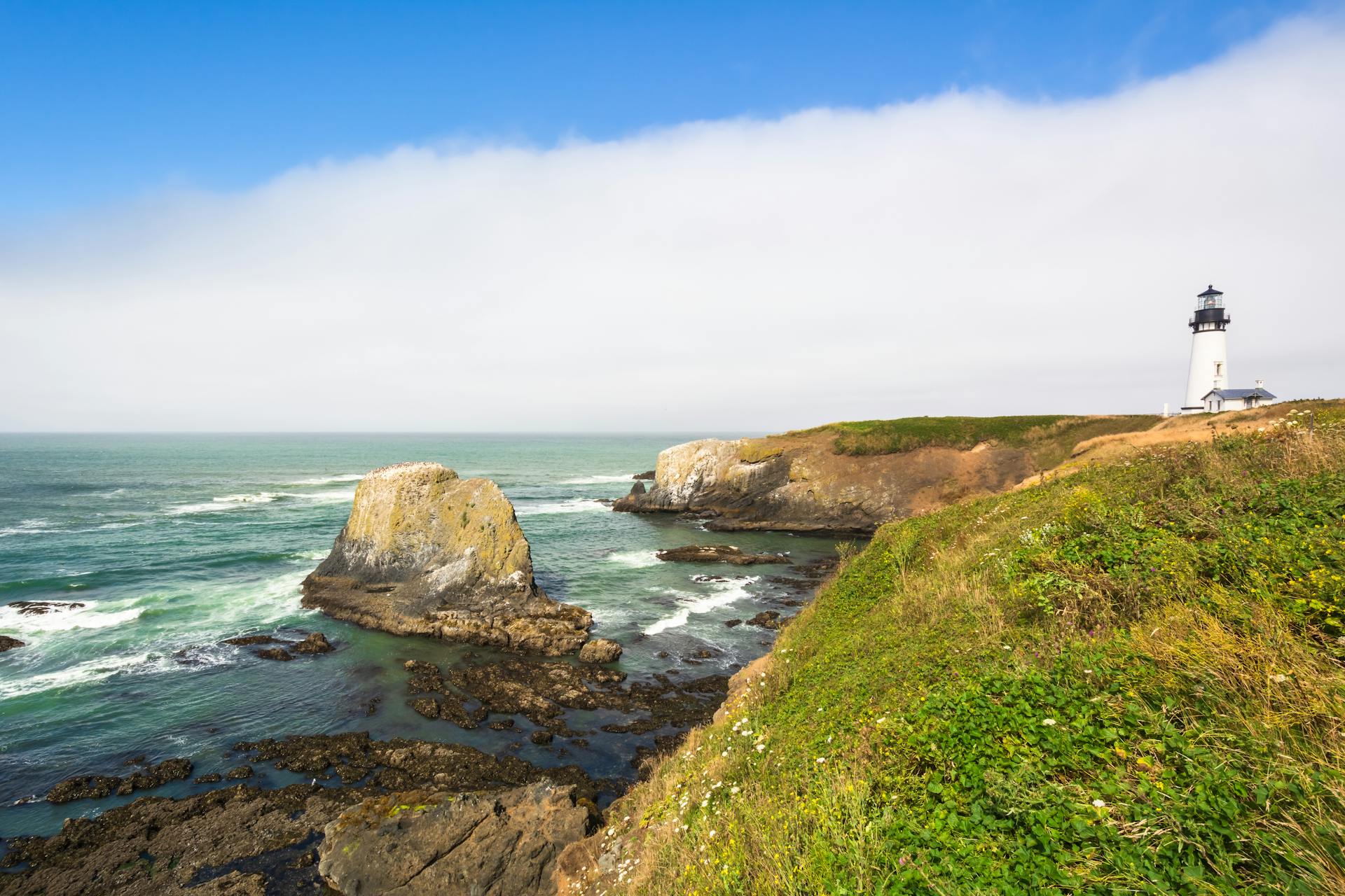 Beautiful Oregon coastline featuring rugged cliffs and a lighthouse against a blue sky.