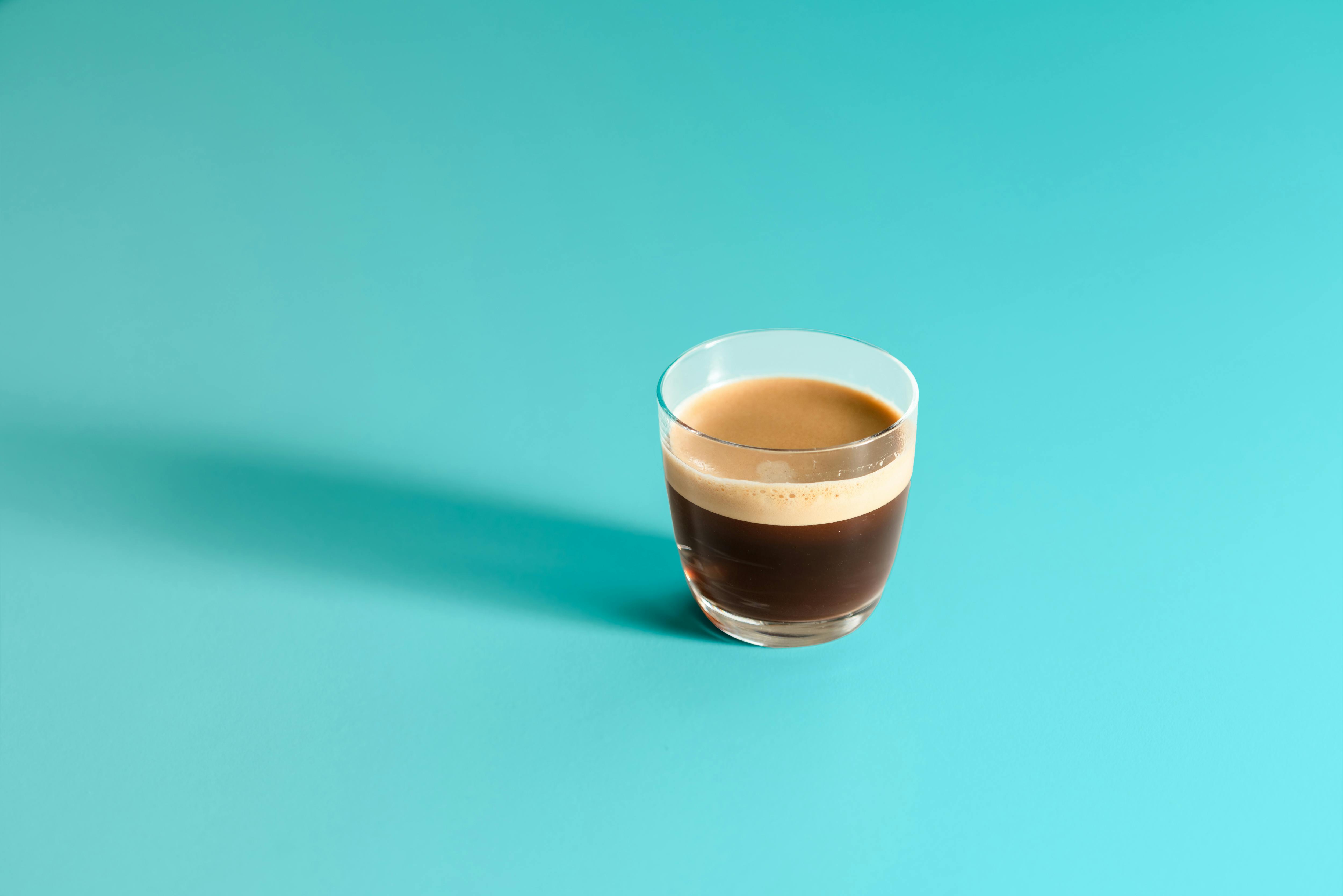 Close-up of a glass cup with espresso on a vibrant turquoise background, showcasing simplicity and elegance.
