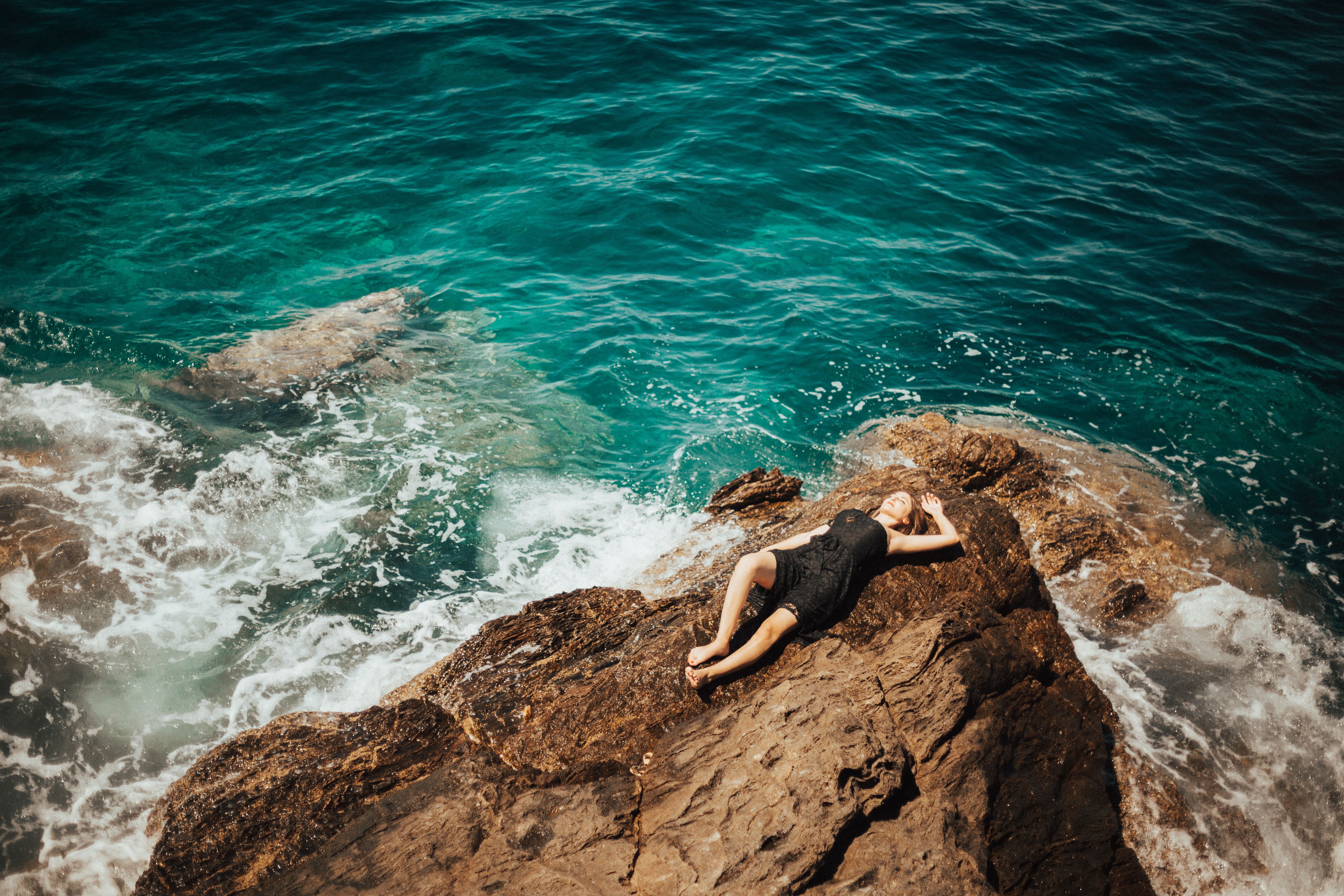 A Woman in Black Dress Lying on Brown Rock · Free Stock Photo