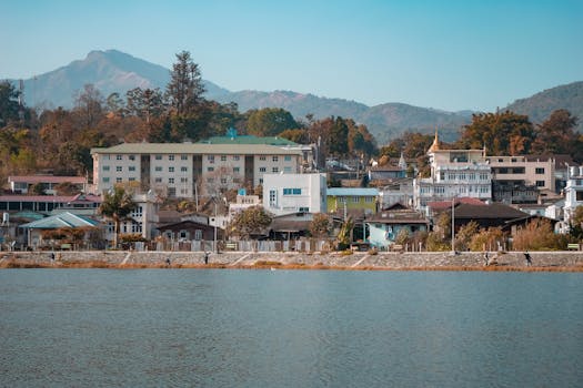 Picturesque waterfront cityscape in Mogok, Myanmar, with colorful buildings and mountain backdrop.