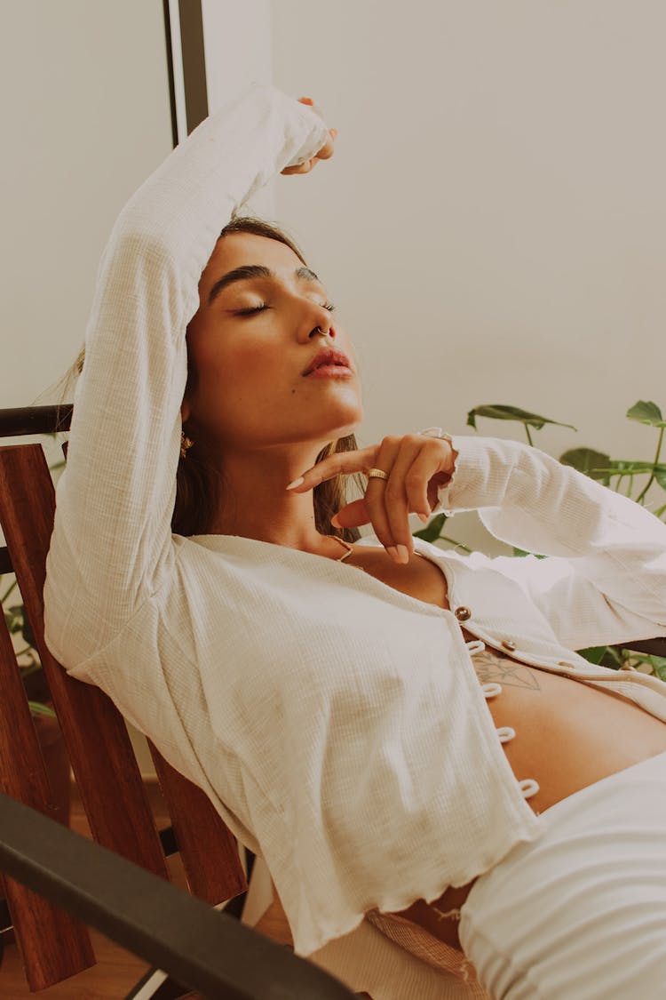 Yung Woman In White Long Sleeve Crop Top Reclining And Relaxing On A Wooden Chair