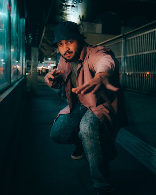 A Man in Brown Long Sleeves Sitting while Posing on the Street at Night