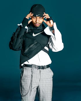 Man in trendy winter clothing posing with hands on cap in a studio setting against a blue backdrop.