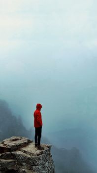 Person in red jacket standing on a foggy mountain cliff, creating a sense of solitude and adventure.